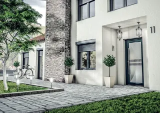 Entrée moderne d'une maison avec façade en pierre, porte vitrée, et jardin soigné.