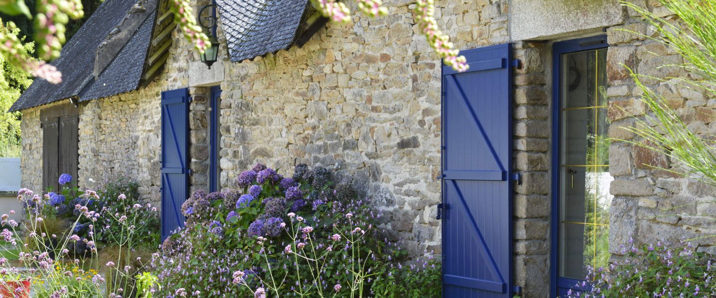 Volets battants bleu sur facade en pierre et fleurie