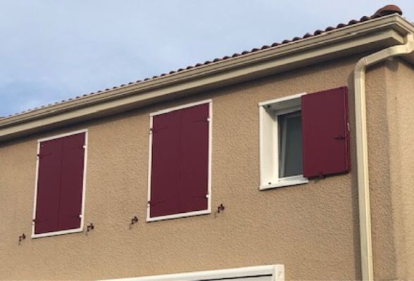 Menuiseries de qualité : fenêtres PVC blanches et volets battants isolants en aluminium rouges.