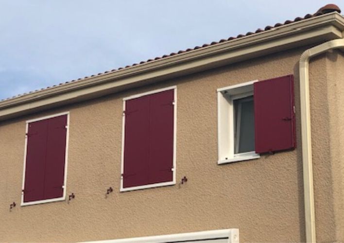 Menuiseries de qualité : fenêtres PVC blanches et volets battants isolants en aluminium rouges.